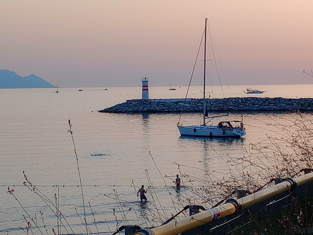 Gün batımında Kuşadası'nda deniz feneri ve demirli yelkenli